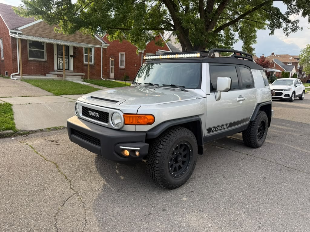 Silver Toyota FJ Cruiser with a roof rack, light bar, and black off-road wheels.